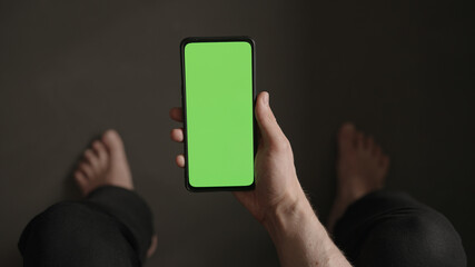 Poster - POV top view shot of man show phone with green screen indoor sitting on a couch