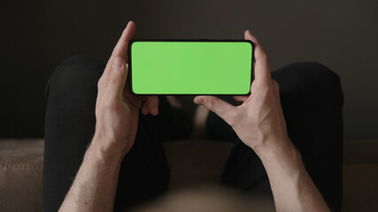 Poster - POV top view shot of man show phone with green screen indoor sitting on a couch