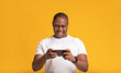© Prostock-studio - Happy glad middle aged muscular attractive african american guy in white t-shirt playing on smartphone