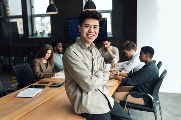 young asian businessman sitting on desk and posing