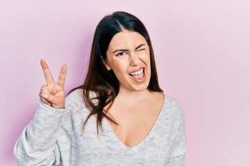 Sticker - Young hispanic woman wearing casual clothes smiling with happy face winking at the camera doing victory sign. number two.