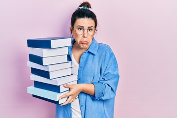 Poster - Young hispanic woman wearing glasses and holding books depressed and worry for distress, crying angry and afraid. sad expression.