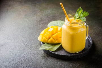 Wall Mural - Refreshing and healthy mango smoothie in a glass with fresh fruit over stone background with copy space