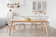 Light scandinavian kitchen interior. White furniture with various utensils, wooden table and chairs in dining room