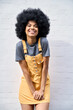 © insta_photos - Portrait of joyful stylish black African American teenage hipster girl wearing trendy yellow sundress with afro hair standing against white bricks wall background smiling looking at camera.
