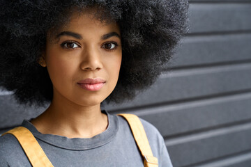 Closeup of young beautiful African American girl of 20s standing on black wall background. Headshot of stylish serious black teenage student with curly hair looking at camera.