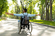 Back view of young disabled black man in wheelchair spreading his arms, feeling happy and free on walk at city park