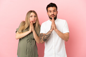 Wall Mural - Pregnant woman and man over isolated pink background pleading