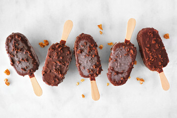 Poster - Chocolate dipped ice cream pops with nuts. Top view scattered on white marble background.