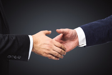 Handshake of two businessmen on a black wall background, partnership concept, close up