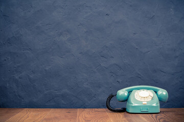 Fototapete - Retro rotary telephone on table front textured black concrete wall background. Vintage old style filtered photo