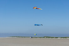 Huge Kites Flying In A Lbue Sky On The Beach With A Van Life Bus Parked Underneath