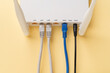 © Maryia - White Wi-Fi wireless router with connected network and power cables on a yellow background. Home and office wlan router with inserted internet cables. Internet hardware close-up.