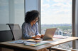 © insta_photos - Happy smiling African American businesswoman executive manager sitting at desk working typing on laptop computer in contemporary corporation office with panoramic view. Business technologies concept.
