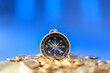 Business, Money Direction and Planning Concept. Closeup of vintage compass on pile of gold coins with blue background.