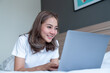 © T-REX - Asian woman lying down and smiling the bed and laptop