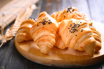 French croissant with black sesame seeds on wooden background, morning breakfast