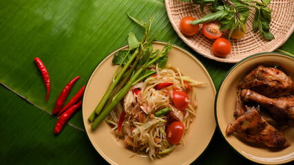 Somtum or papaya salad and Thai style grilled chicken on banana leaves background