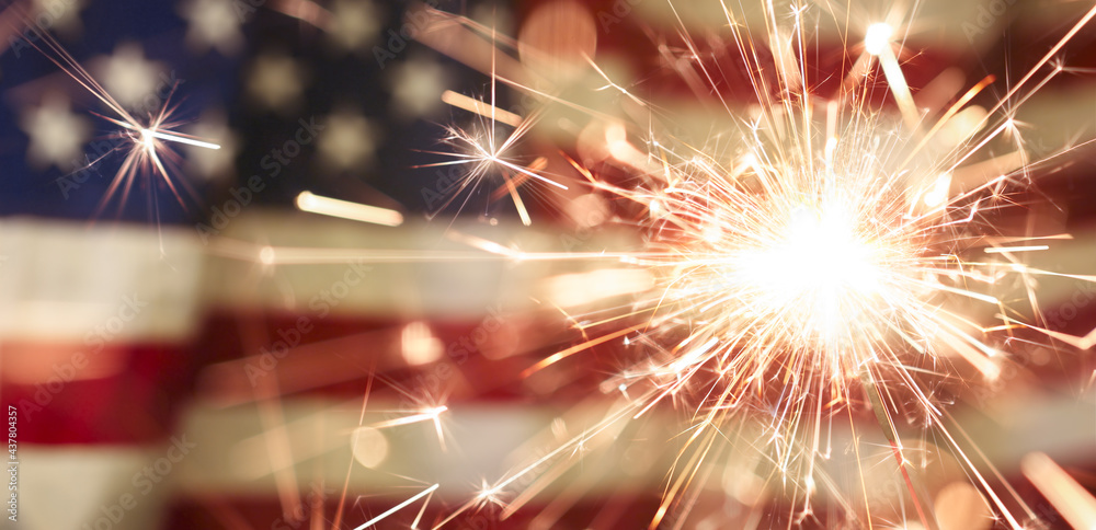 Sparks flying off a burning sparkler in front of the US American flag for patriotic 4th of July celebration. - obrazy, fototapety, plakaty 