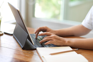 Side view of female hands typing on digital tablet keyboard on the table with stationery