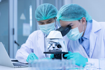 asian man scientist looking sample blood with microscope doing experiment about coronavirus vaccine 