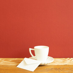 Wall Mural - White coffee cup and envelope on wooden table. red background