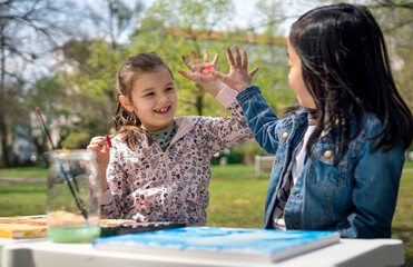 Wall Mural - Small children painting pictures outdoors in city park, learning group education concept.