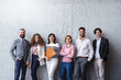 © Halfpoint - Portrait of group of entrepreneurs standing against concrete wall indoors in office, looking at camera.