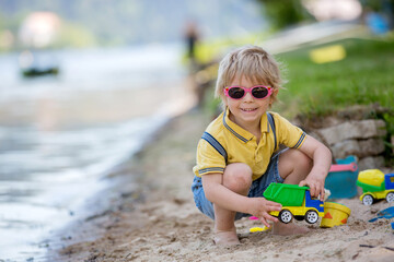 Little toddler child, cute boy, playing with toys in the sand on a lake