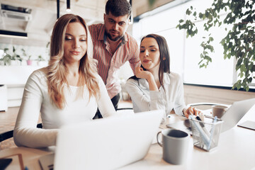 Wall Mural - Two female and one male business partners looking at computer screen and discussing their project