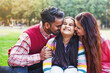 Cute Indian little girl being kissed by both of her parents on the cheeks outdoor in the park