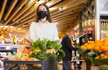 Portrait of a young girl in a protective mask with a full grocery cart, who came to the supermarket for shopping ..during the pandemic