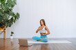 © Olga - Attractive young woman sit in lotus yoga position in light room with laptop and have online lesson. Relaxing state of mind, meditation.