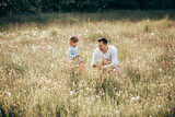 Fototapeta Kuchnia - Young dad spends time with his little son in nature, collecting bouquet for mom from wildflowers, single father