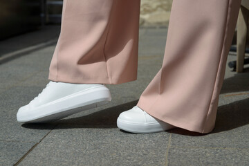 Wall Mural - Stylish woman in fashion white sneakers shoes and beige trousers walks around the city.