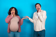 © Roquillo - Crazy young couple expecting a baby standing against blue background advising discount prices hold open palm new product