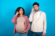 © Roquillo - young couple expecting a baby standing against blue background tries to memorize something, keeps fore finger on temple, reminds information for exam,