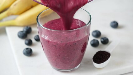 Wall Mural - Pouring blueberry smoothie in glass. Thick purple smoothie with acai powder