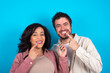 © Roquillo - young couple expecting a baby standing against blue background holding an invisible aligner and pointing to her perfect straight teeth. Dental healthcare and confidence concept.