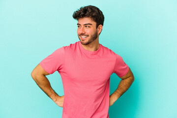 Wall Mural - Young caucasian man isolated on blue background laughs and closes eyes, feels relaxed and happy.