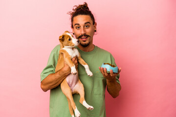 Young caucasian man holding his puppy and his food isolated on pink background