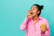 © Asier - Young latin woman holding chips isolated on blue background shouting and holding palm near opened mouth.