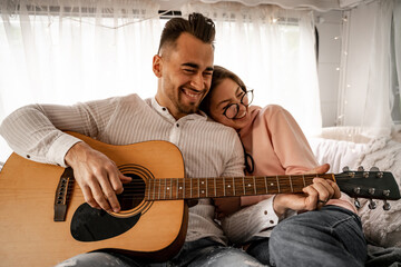 cheerful man playing acoustic guitar near laughing woman in trailer