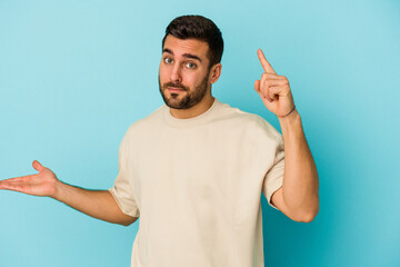 Young caucasian man isolated on blue background holding and showing a product on hand.