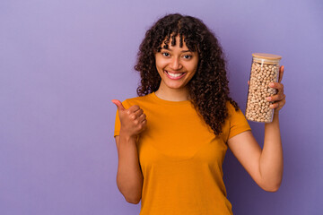 Wall Mural - Young brazilian woman holding a chickpea bottle isolated on purple background smiling and raising thumb up