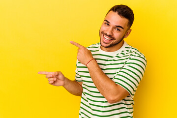 Young caucasian man isolated on yellow background pointing with forefingers to a copy space, expressing excitement and desire.