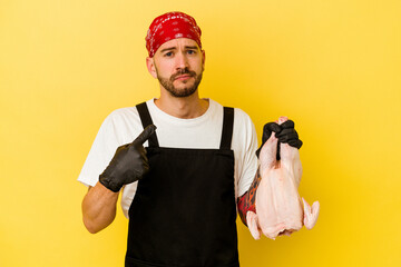 Wall Mural - Young tattooed batcher caucasian man holding a chicken isolated on yellow background pointing with finger at you as if inviting come closer.