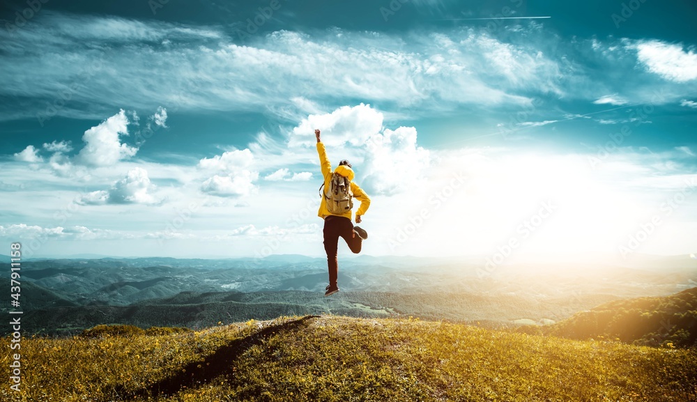 Hiker with backpack raising hands jumping on the top of a mountain ...