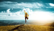 Hiker With Backpack Raising Hands Jumping On The Top Of A Mountain - Successful Man With Arms Up Enjoying Victory - Sport And Success Concept