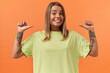 Cheerful pretty young woman in yellow tshirt smiling and pointing at herself by thumbs at both hands isolated over orange background
